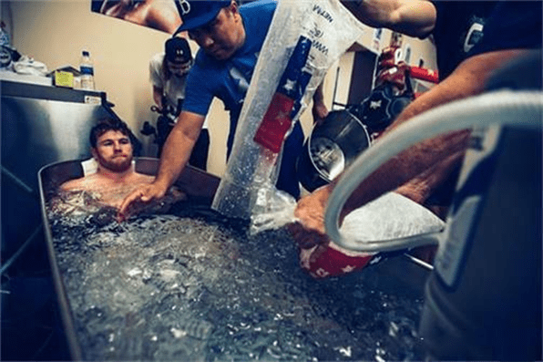 An athlete undergoes ice bath therapy with help from others